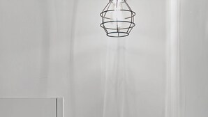 Een slaapkamer met een bed, een nachtkastje met lades en een hanglamp.