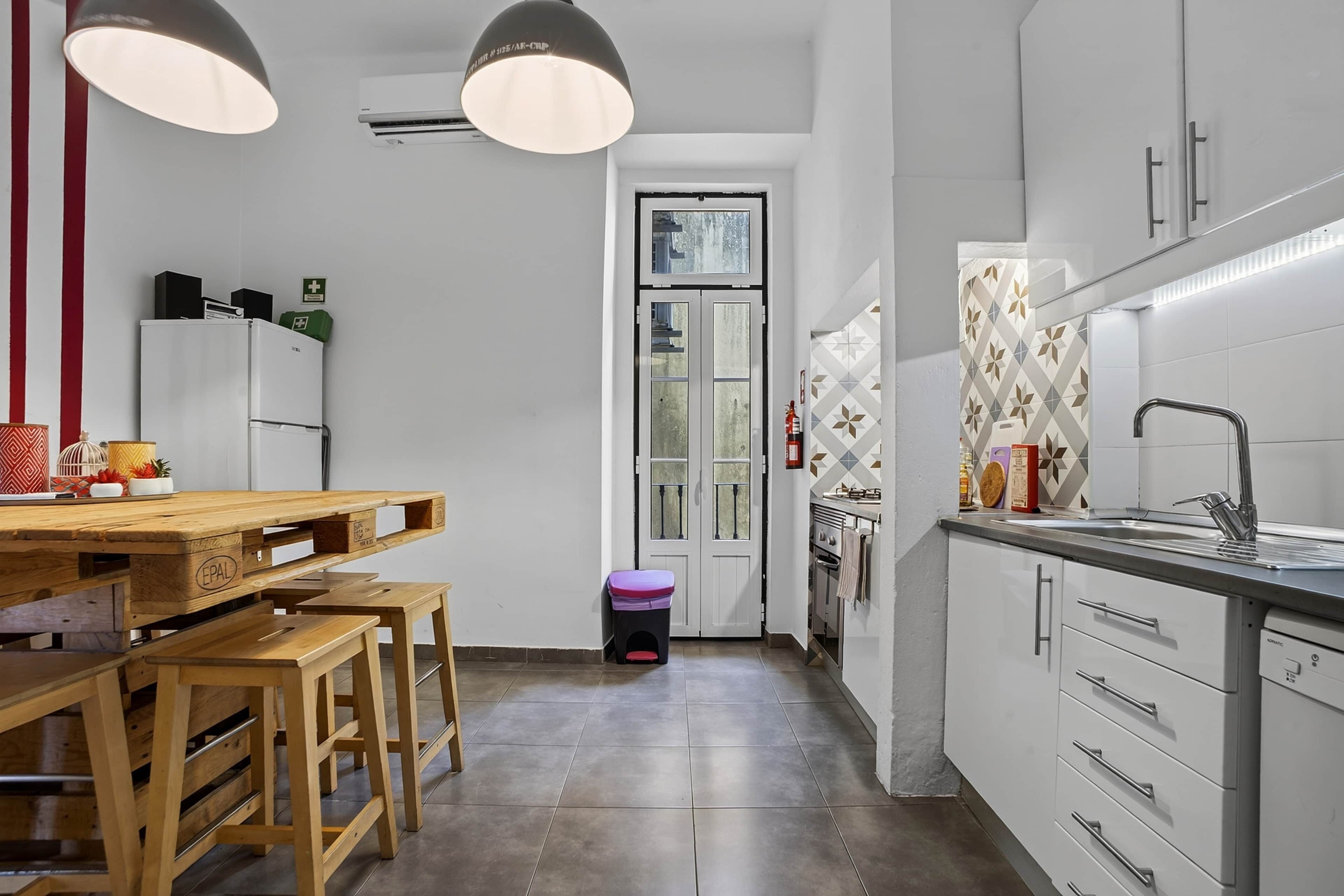 Une cuisine moderne avec une table à manger en bois, deux lampes suspendues, un four encastré et un évier avec un robinet.