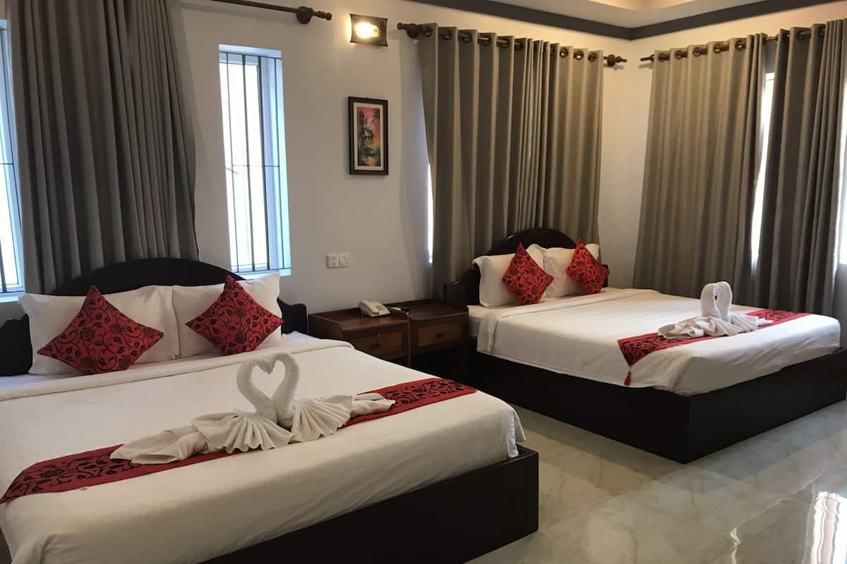Deux lits doubles avec du linge de lit blanc, des coussins à motifs rouges et une décoration en forme de cœur faite avec des serviettes.