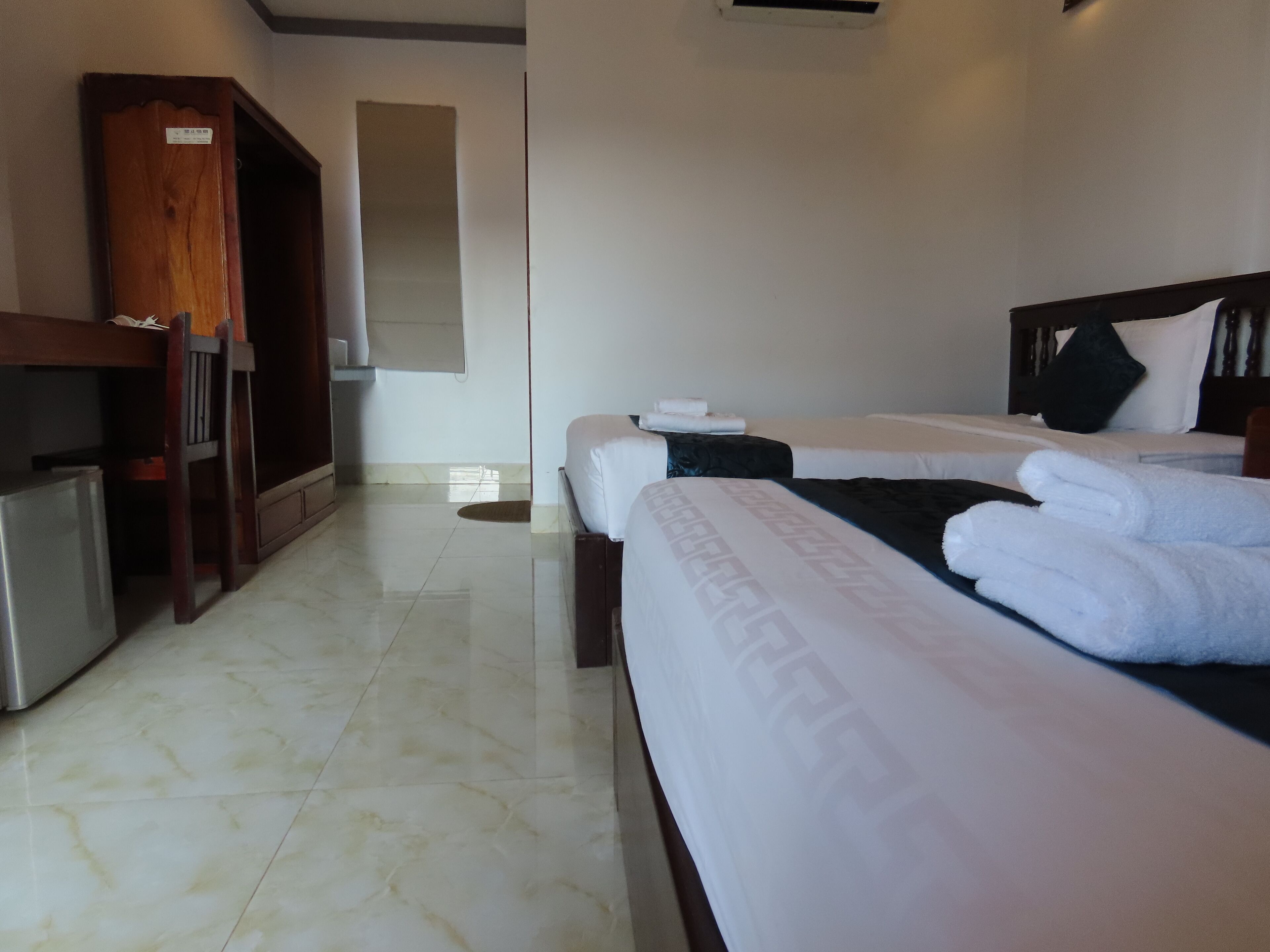 A hotel room with two beds, a desk, and a refrigerator.