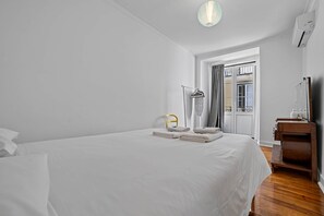 A hotel room with a large bed, a wooden dresser, a hanging light fixture, and a view through a door.