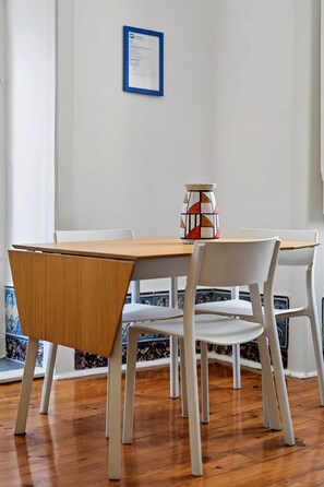 Uma sala de jantar com mesa de madeira e cadeiras brancas, um vaso decorativo e um documento emoldurado na parede.