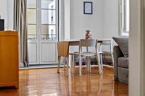 A room with a wooden floor, a dining table with chairs, a sofa, and a wall-mounted picture frame.