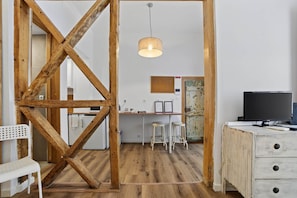 A room with exposed wooden beams, a desk with two stools, a television, and a hanging light fixture.