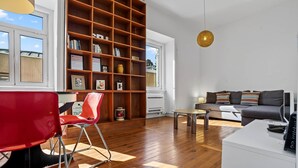 Un salon moderne avec une grande bibliothèque en bois, un fauteuil rouge, un canapé gris et une table ronde.
