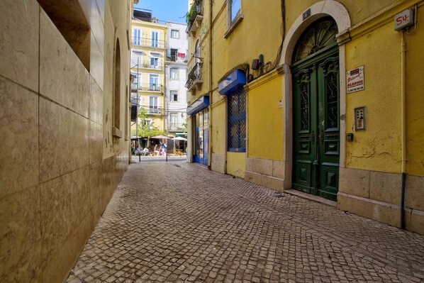 A narrow cobblestone street with buildings on either side, a green door, and a sign indicating a business. - Saint Paul, Third Floor (Lisboa)
