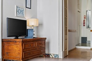A wooden dresser with a flat-screen TV and a lamp, a framed 'HOME' sign on the wall, and a fire extinguisher mounted on the wall. - Lively Bairro Alto, in the heart of the nightlife district (Lisboa)