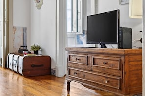 Ein Holzkoffer mit einem Fernseher darauf, einem Koffer und einer Pflanze in einem Zimmer mit Holzboden und einem Fenster.