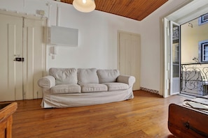 Ein Zimmer mit Holzboden, einem beigen Sofa und einer weißen Decke.