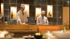 Un restaurant avec deux serveurs qui servent les plats. Les murs sont ornés de tableaux encadrés et il y a un comptoir en bois.