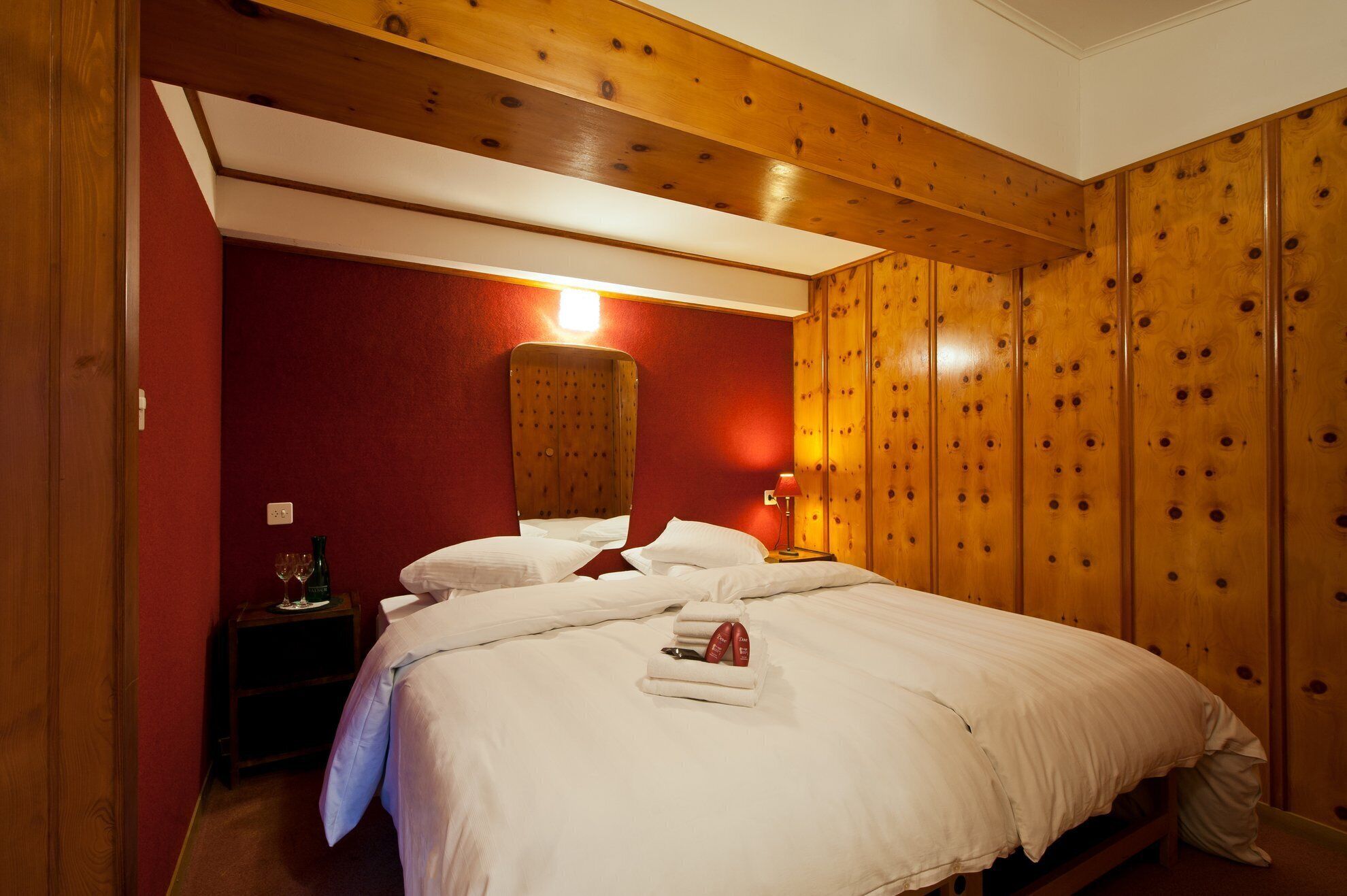 A hotel room with a wooden ceiling, a red accent wall, and a bed with white linens.