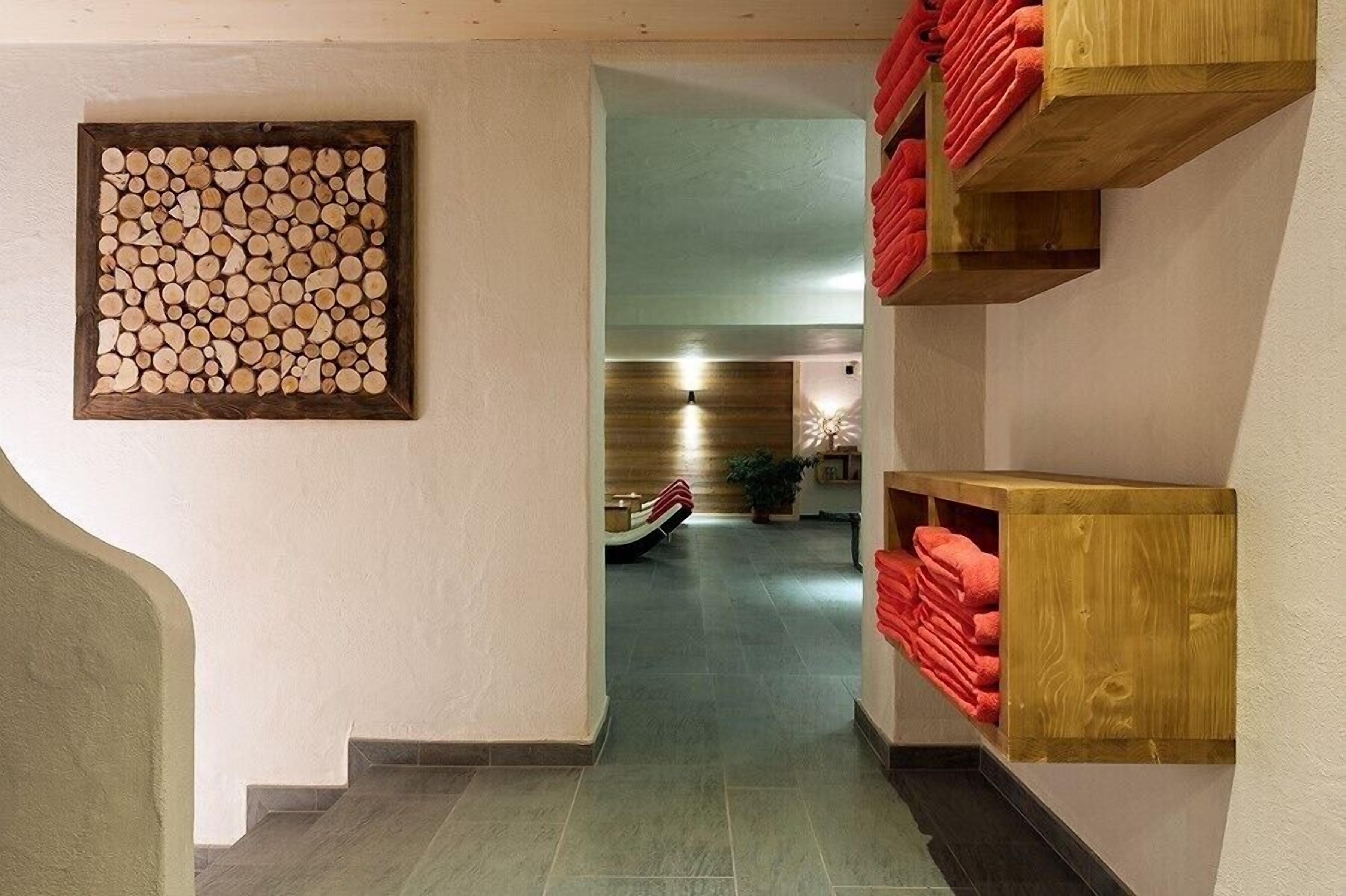 A hallway with a wooden log wall art, a staircase with red towels, and a wooden cabinet.