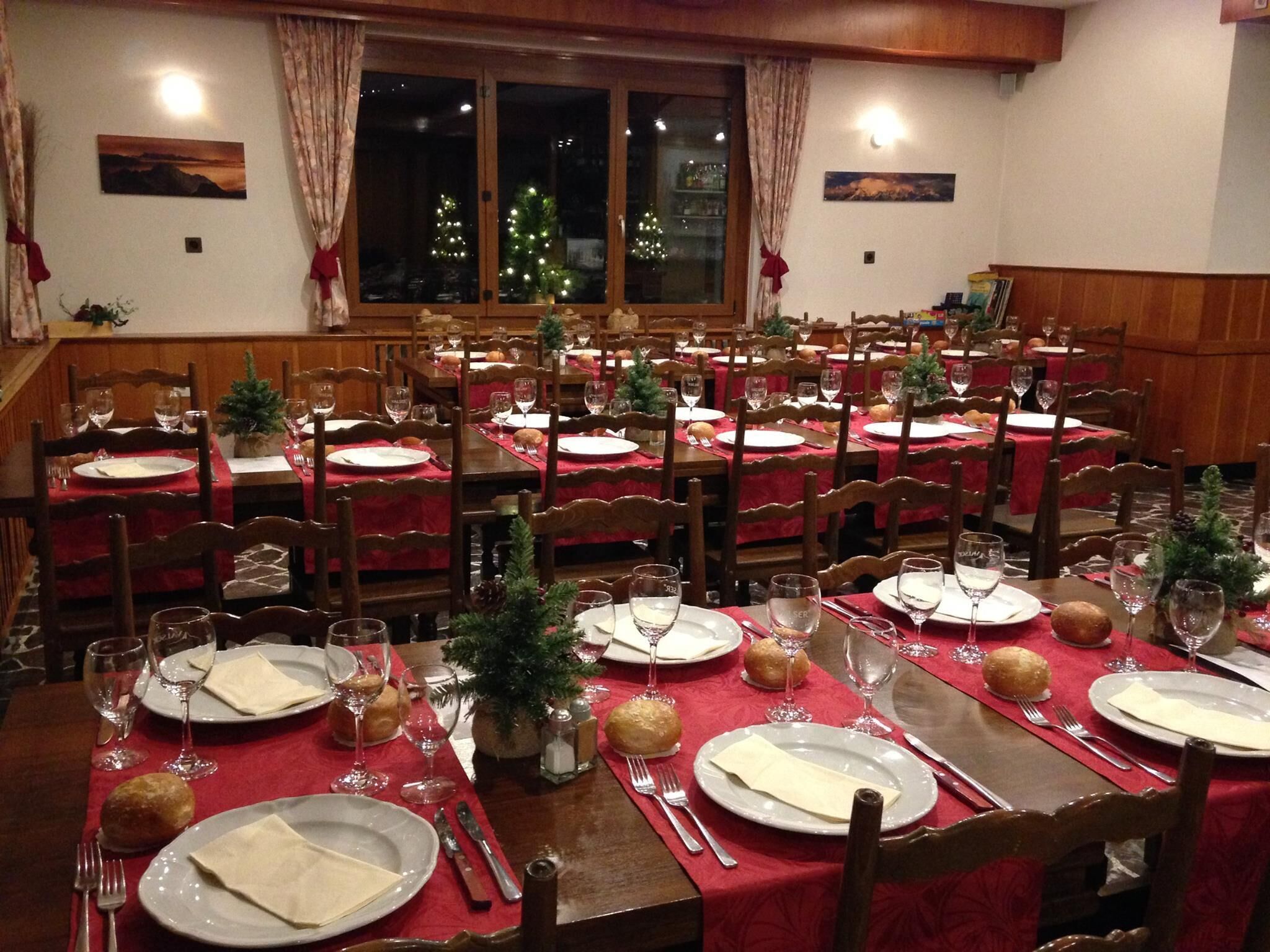 A dining area with multiple tables set for a meal, featuring red tablecloths, wooden chairs, and Christmas decorations.