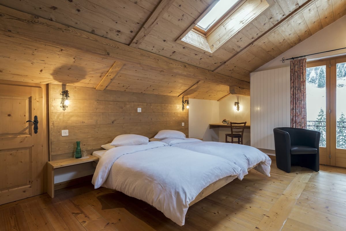 Ein Zimmer mit Holzboden, einem Bett, einem Schreibtisch und einem Sessel.
