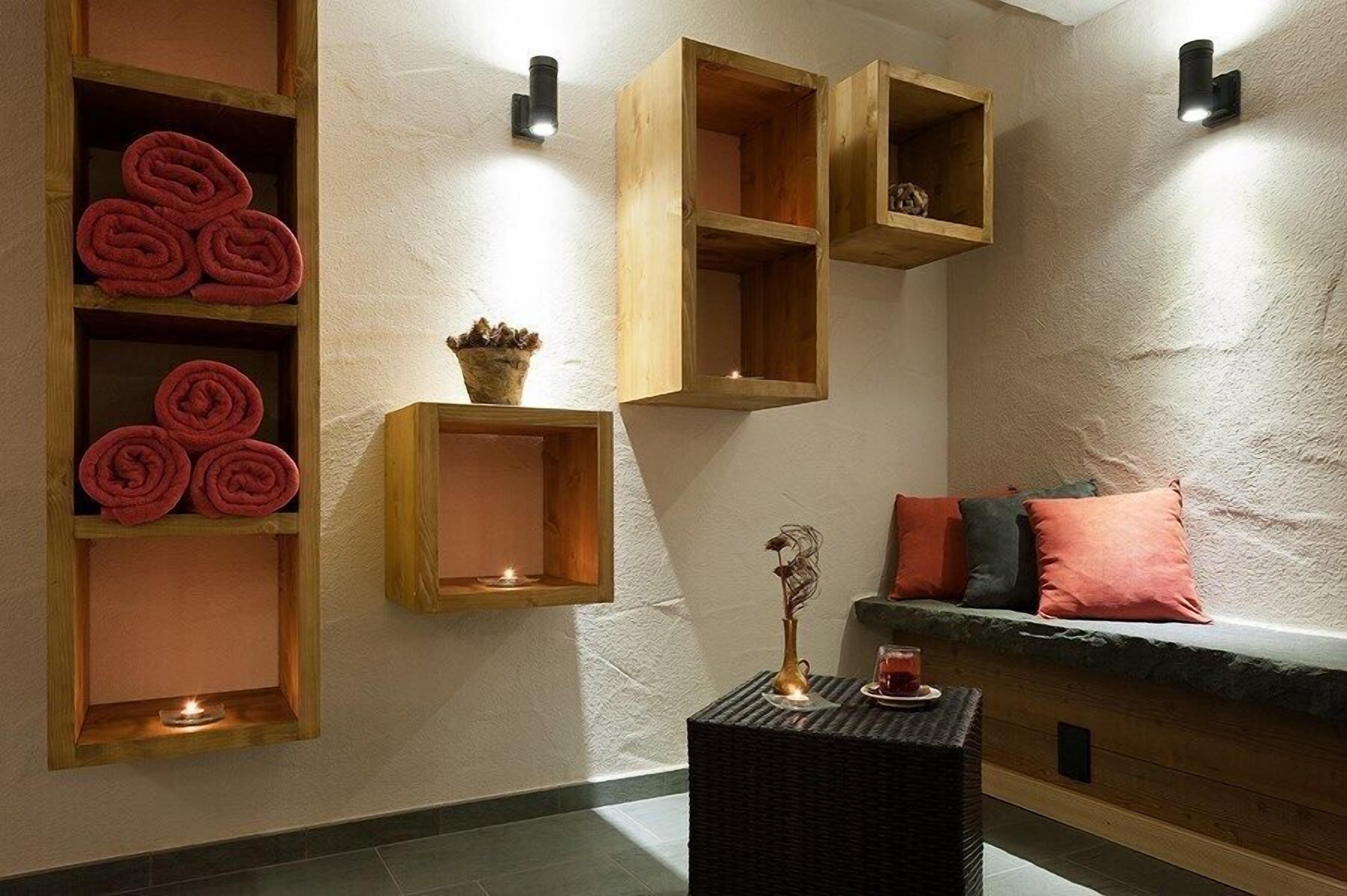 Une pièce aménagée comme un spa, avec des étagères en bois où sont rangées des serviettes pliées, une petite table sur laquelle est posé un vase, et un banc rembourré agrémenté de coussins.