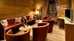 A cozy room with wooden walls and ceiling, furnished with leather sofas, armchairs, and a small round table. - La Vallée Hotel & Spa (Bagnes)
