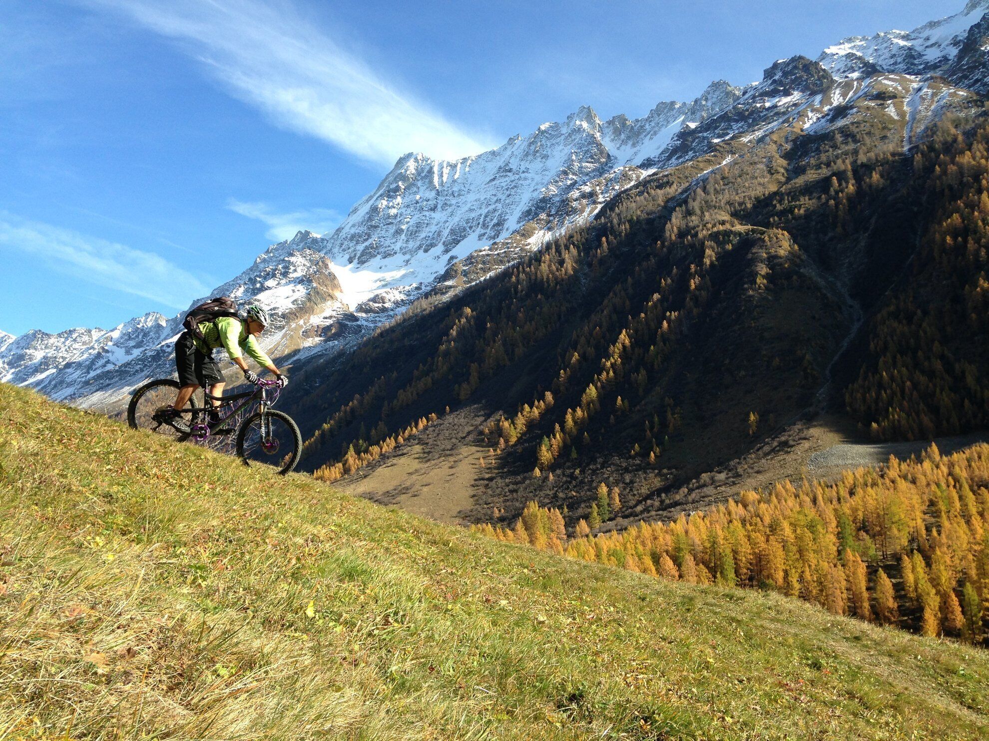 A mountain biker on a trail with snow-capped peaks in the background.