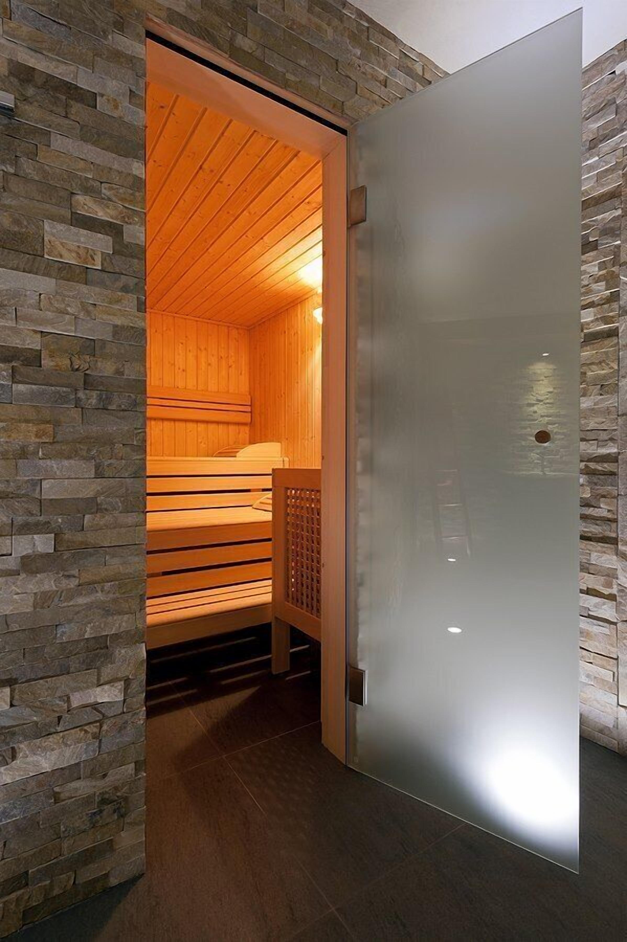 Una sala de sauna con bancos de madera y pared de piedra.