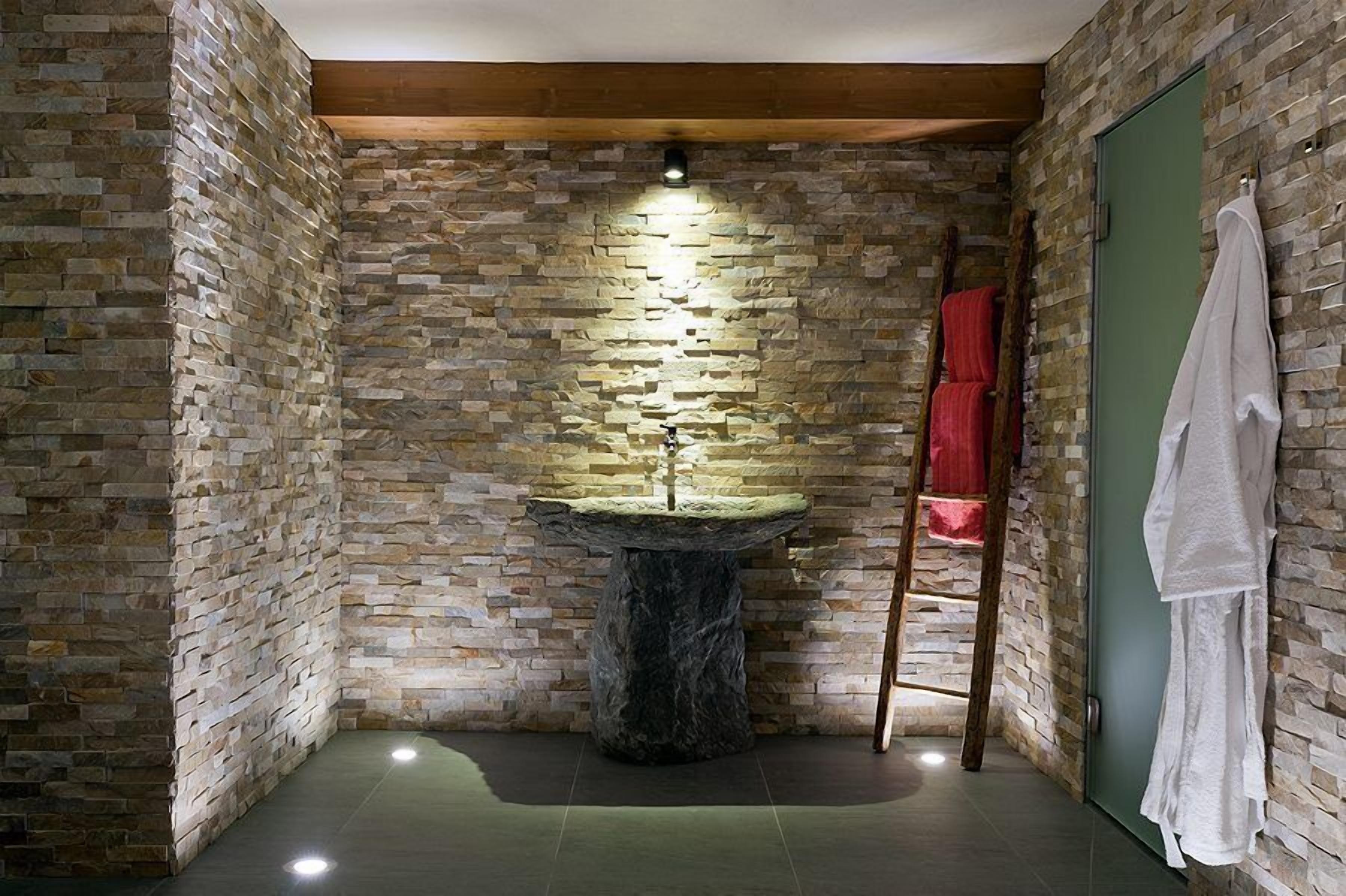A stone-walled bathroom with a central sink, wooden beams, and towels on a rack.