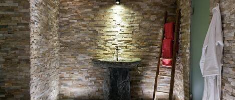 A stone-walled bathroom with a central sink, wooden beams, and towels on a rack.