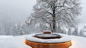 A wooden hot tub surrounded by snow, with a tree in the background. - La Vallée Hotel & Spa (Bagnes)