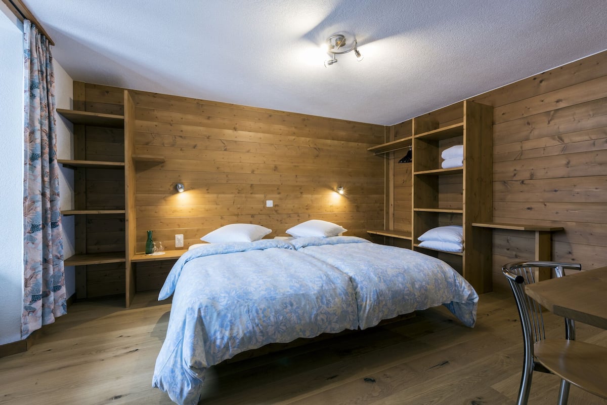 Ein Schlafzimmer mit Holzboden, einem Bett mit Blumenmuster, einem Schreibtisch und eingebauten Regalen.
