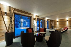 A spa area with wooden walls, a large window with a winter scene, and black wicker furniture.