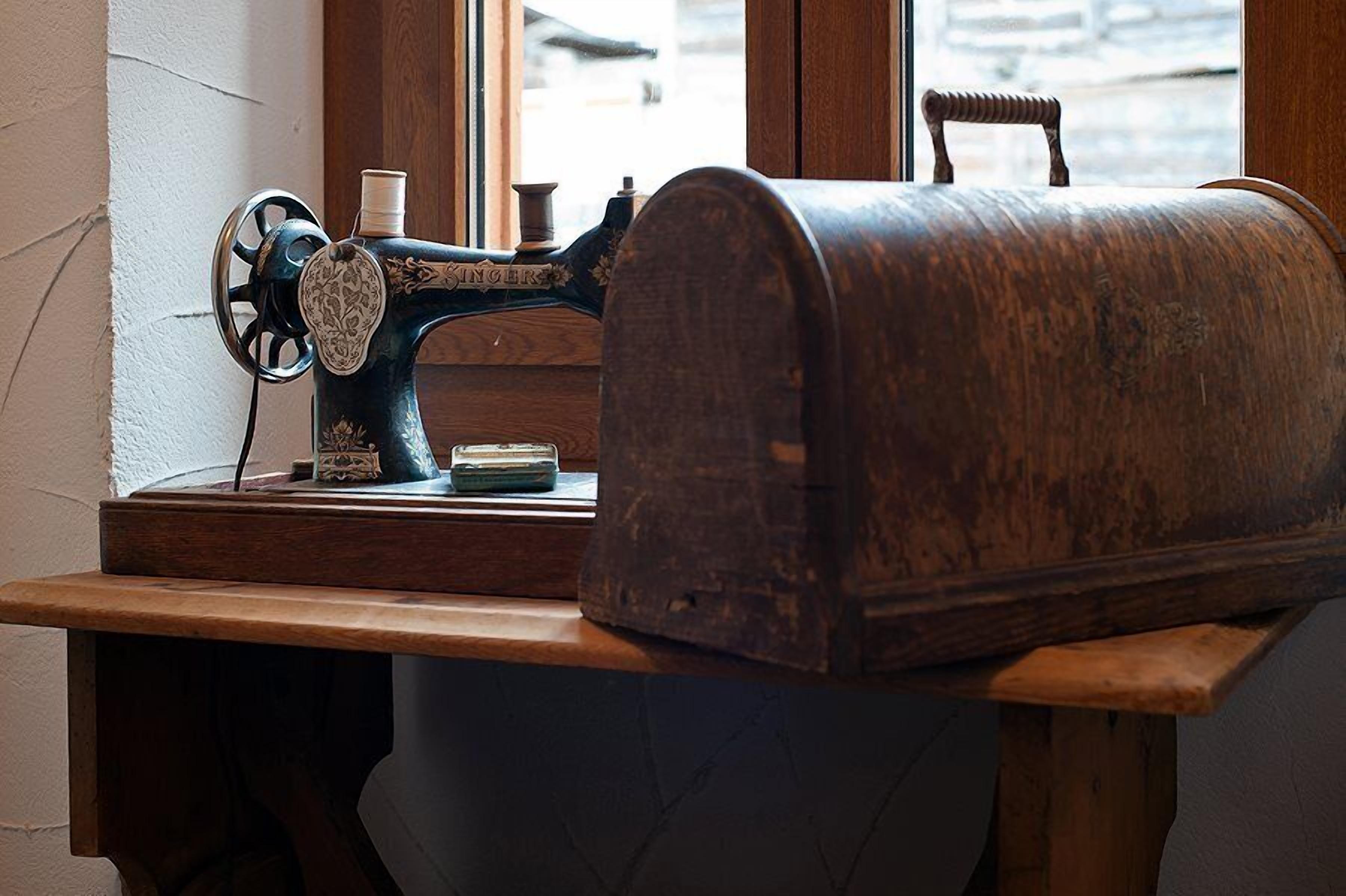 Una máquina de coser Singer antigua sobre una mesa de madera junto a una ventana.