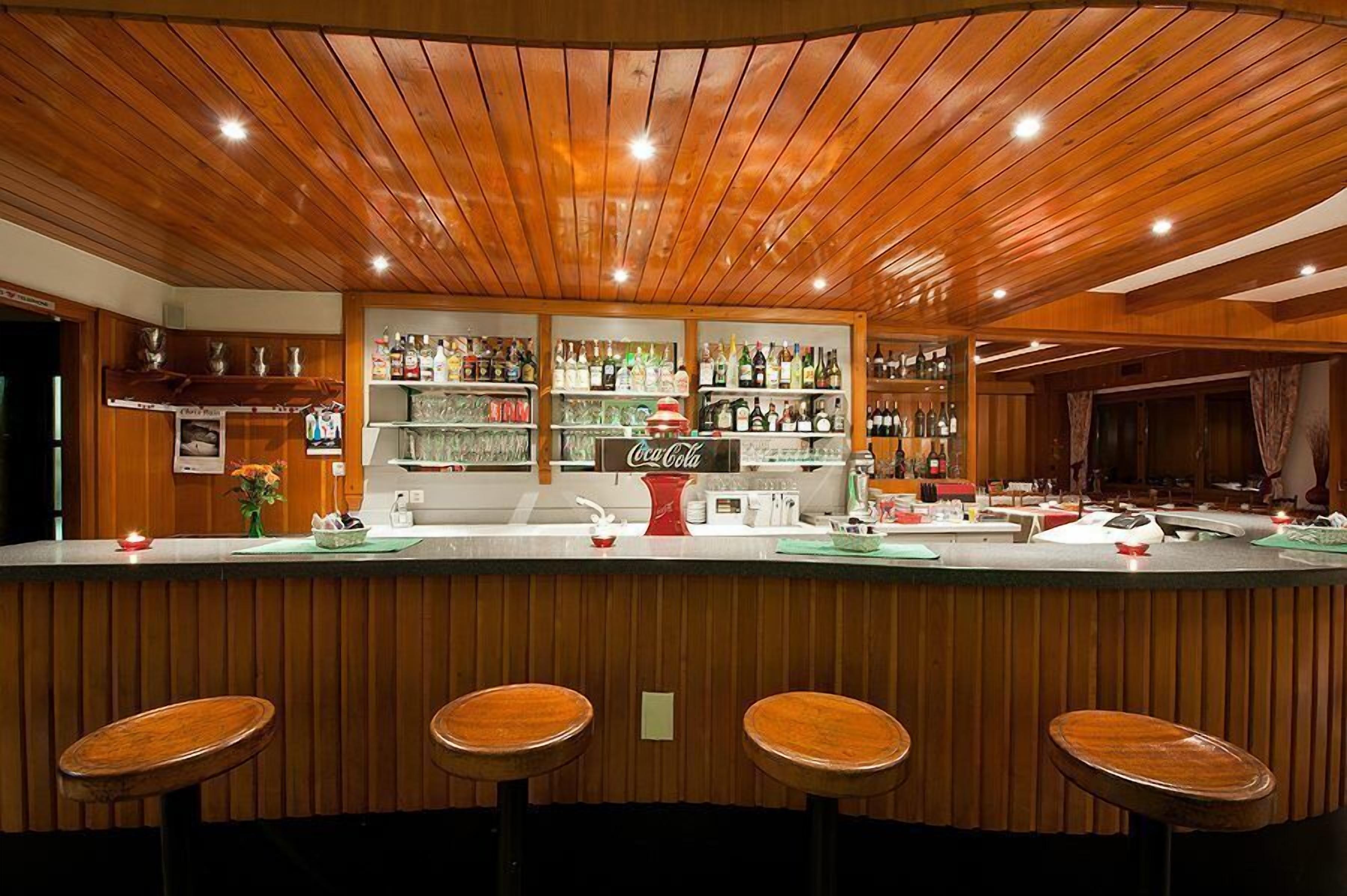 A bar area with wooden paneling, a Coca-Cola sign, and shelves stocked with various bottles.