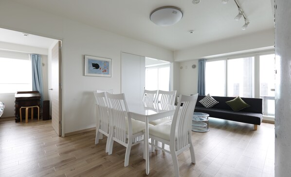 A spacious living room with a dining area, a sofa with cushions, and a painting on the wall. - Herber Light SHINONOME (Otaru)