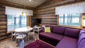 A log cabin interior with a round dining table, white chairs, a purple sofa, and a TV on a wooden stand. - Holiday Club Pyhäniemi (Kihnio)