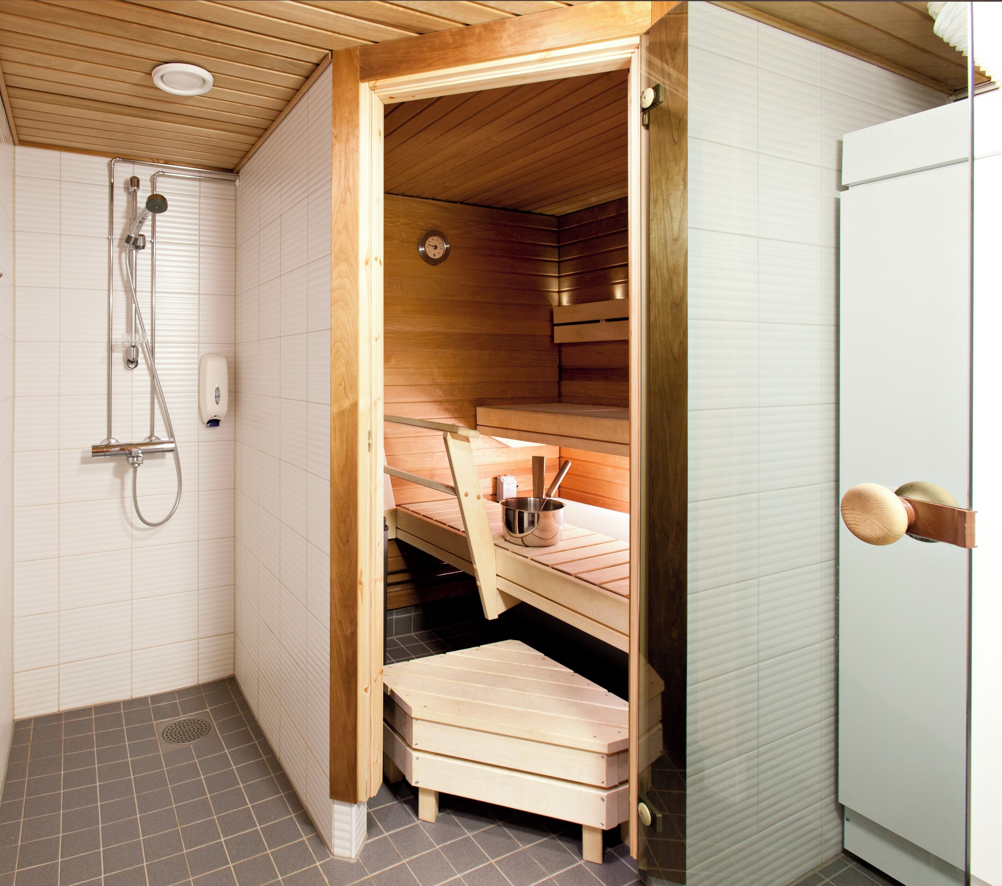 Een sauna met een houten bank, een douchekop en een klein tafeltje met een kom en lepel.