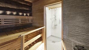 A wooden cabin interior with a sauna, a wooden bench, and a shower area. - Holiday Club Pyhäniemi (Kihnio)