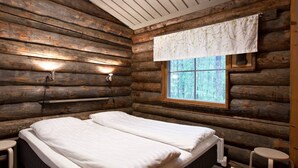 A log cabin bedroom with two beds, a window with a white curtain, and a small stool by the window. - Holiday Club Pyhäniemi (Kihnio)