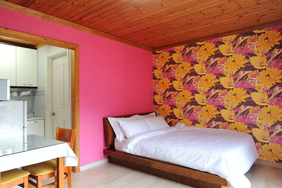 Una habitación con cama, una mesa de comedor con sillas, una zona de cocina y un papel tapiz floral llamativo.