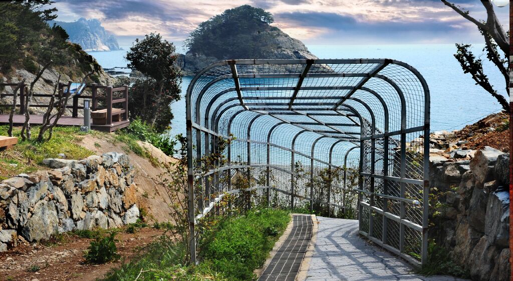 A metal archway leading to a coastal area with a rocky path and a view of the sea.