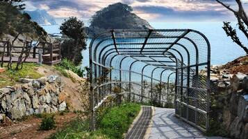 A metal archway leading to a coastal area with a rocky path and a view of the sea.
