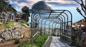 A metal archway leading to a coastal area with a rocky path and a view of the sea. - Geoje Floria Pension (Geoje)