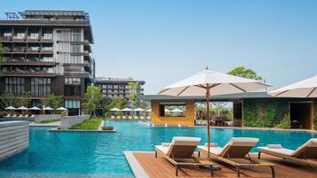 A modern hotel with a swimming pool, lounge chairs, and umbrellas.