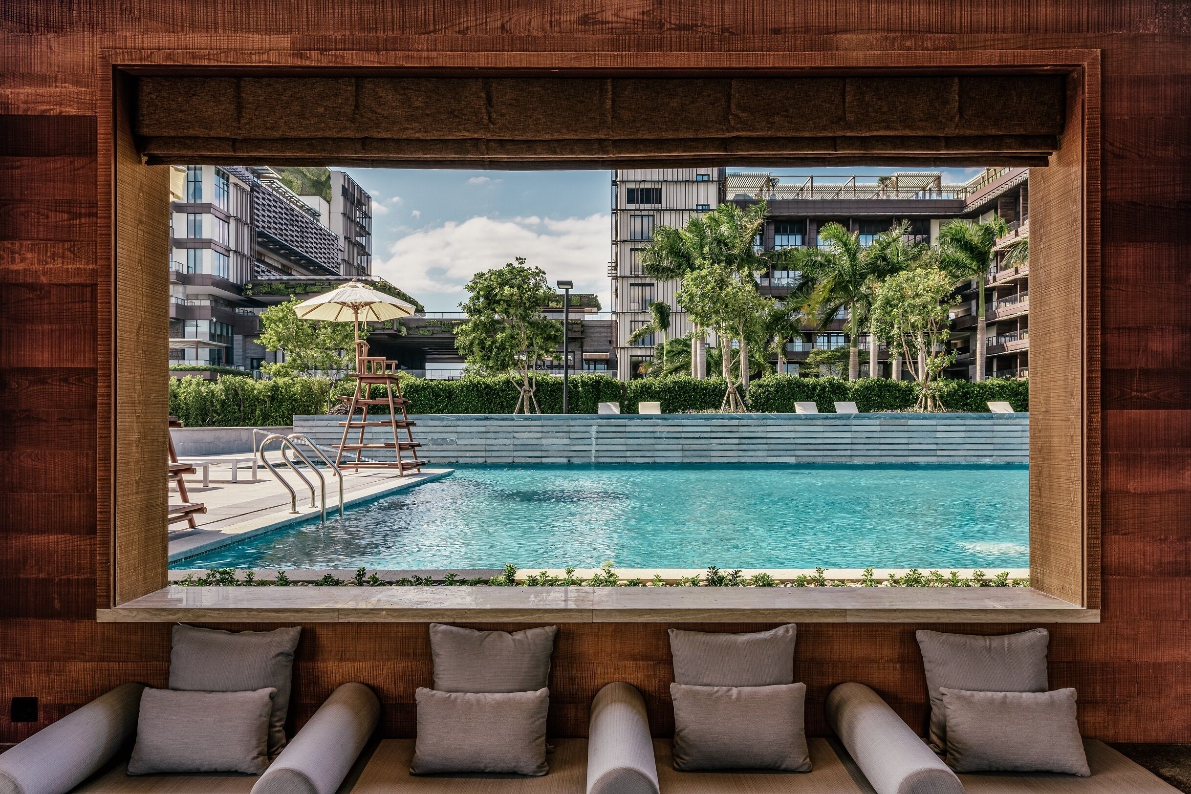 A modern pool area with a view of surrounding buildings, a ladder, and lounge chairs with cushions.