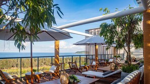 Eine Terrasse mit Holzmöbeln, weißen Sonnenschirmen und Blick auf das Meer.