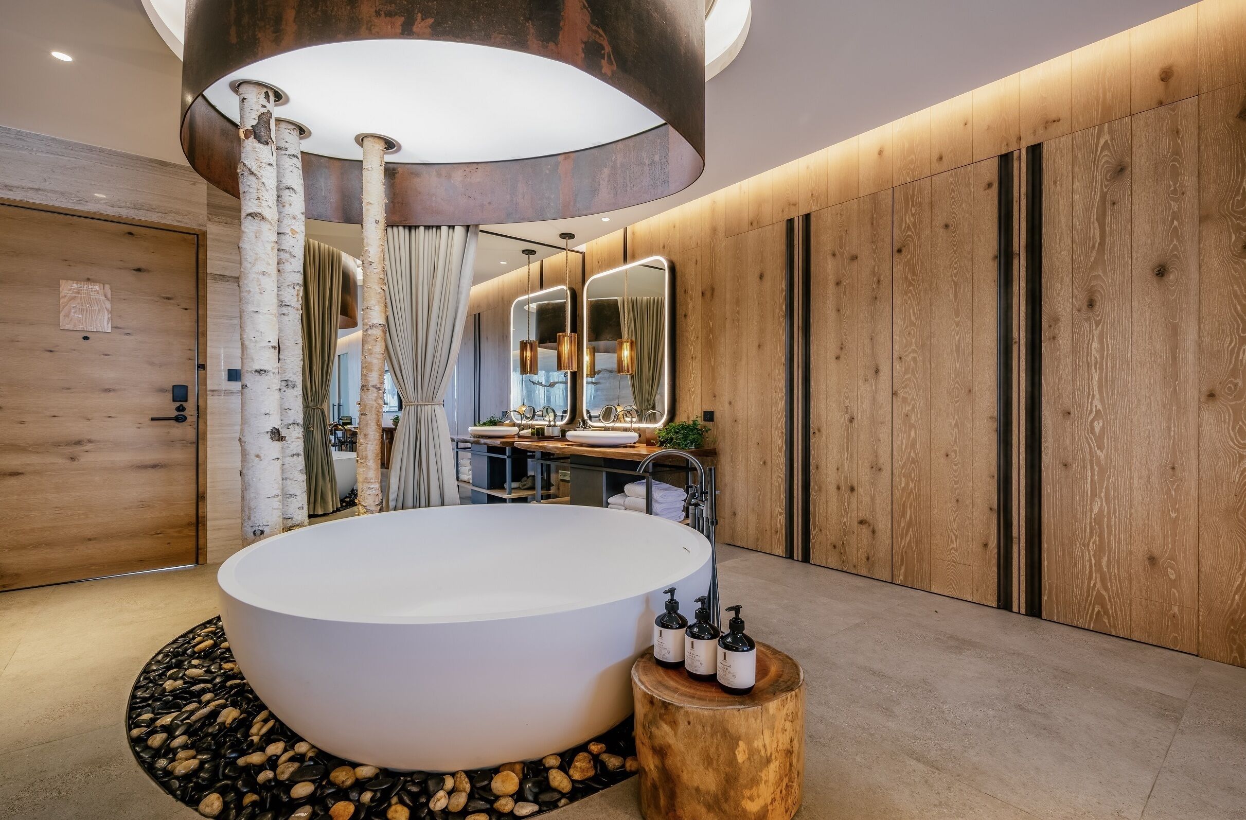 A modern bathroom with a large bathtub, wooden walls, and a round wooden stool with toiletries.