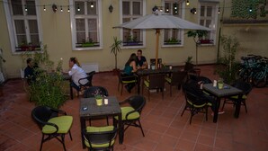 An outdoor patio area with tiled flooring, multiple tables and chairs, string lights, and potted plants. - MP Hostel Budapest (Budapest)