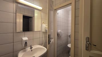 Een badkamer met een wastafel, spiegel, handdroger en toilet.