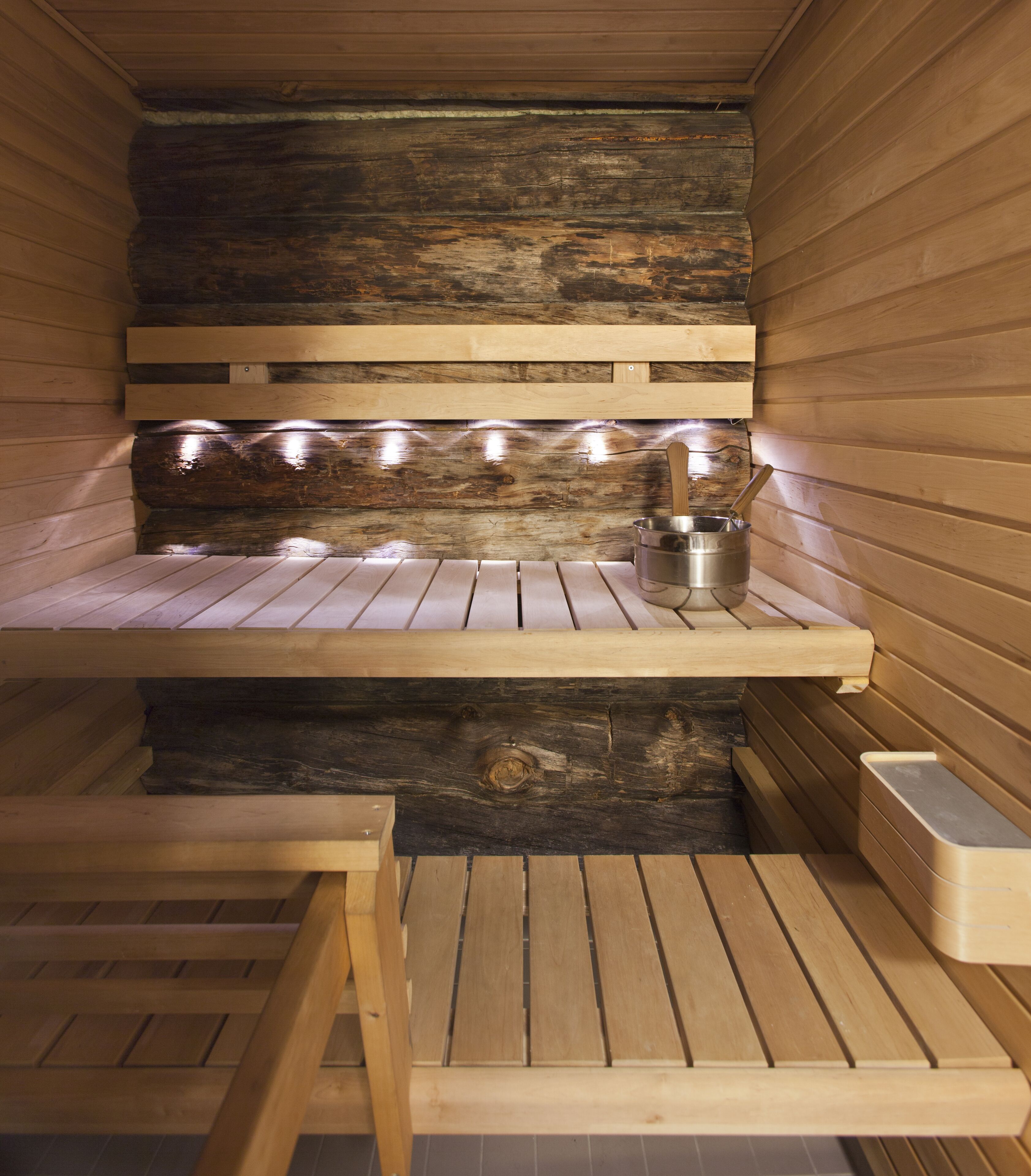 A sauna with wooden benches and a metal container, likely for water or steam.