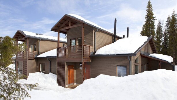 Un chalet moderne à deux étages, doté d’une façade en bois et d’un balcon, entouré de neige.