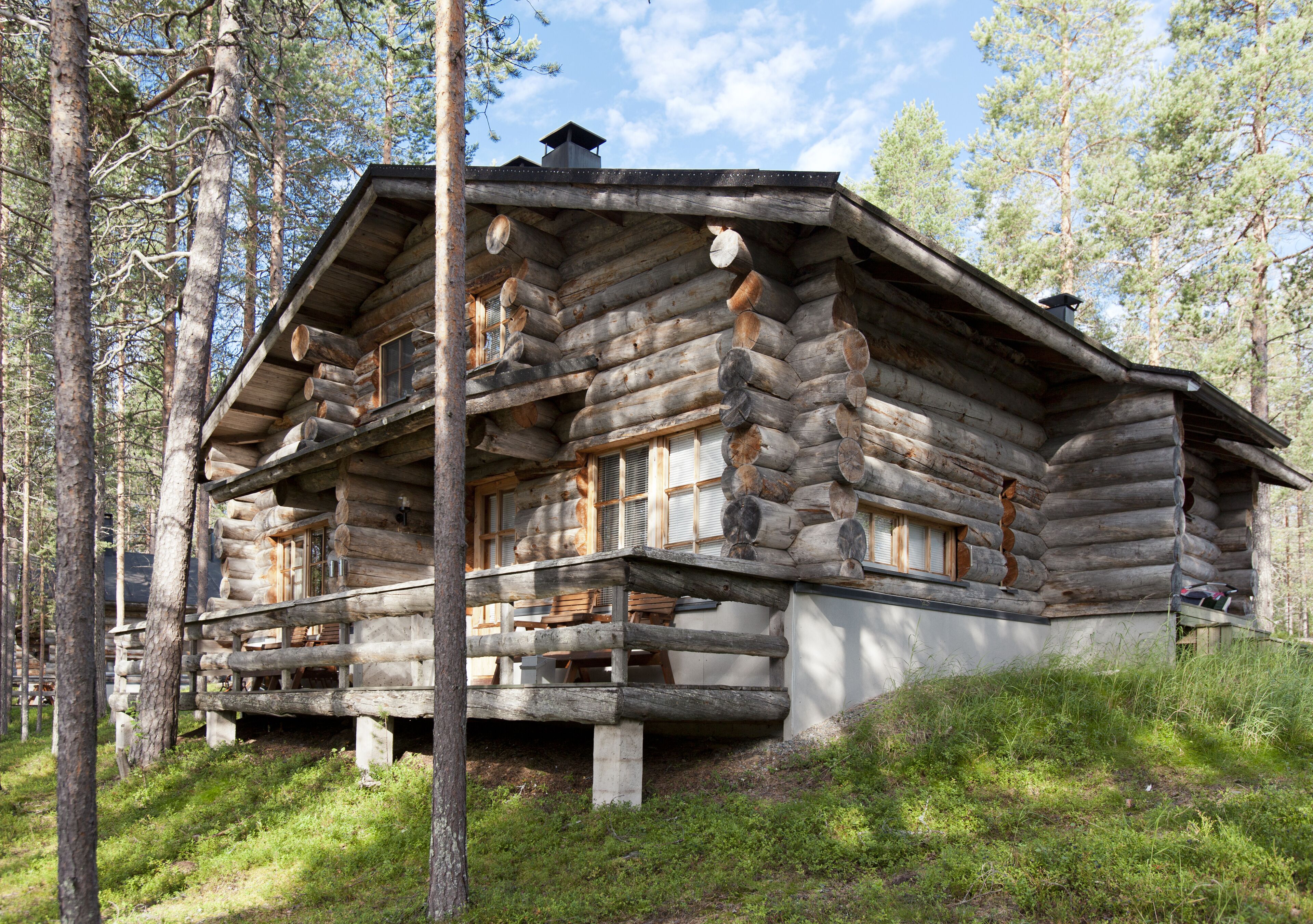 A log cabin with a balcony, surrounded by trees.