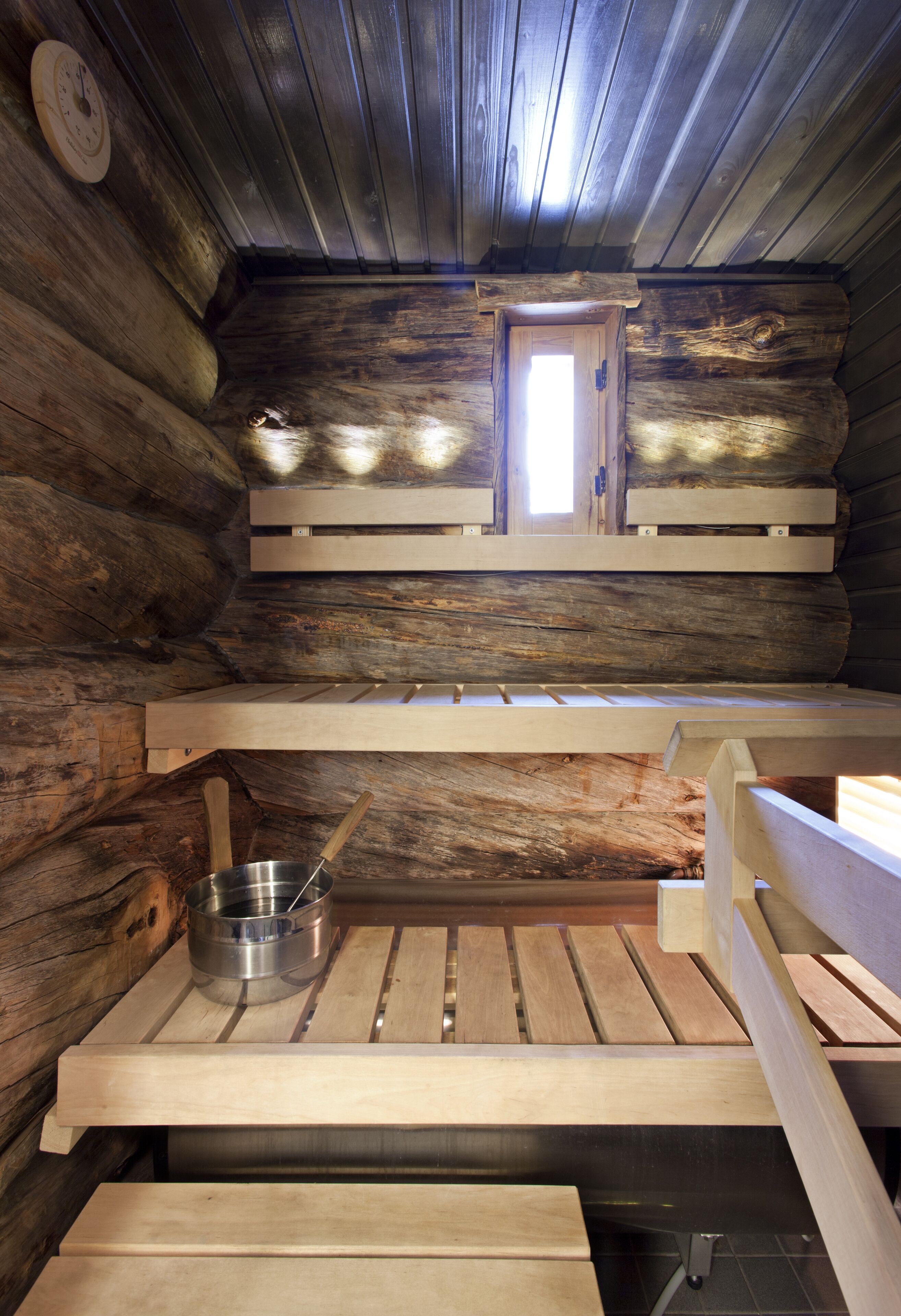 Het interieur van een blokhut, met een sauna bank, een metalen kom en een houten deur.