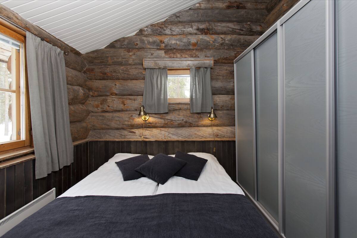 A log cabin bedroom with a bed, curtains, and wall-mounted lights.