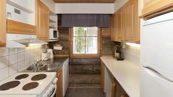 A compact kitchen with wooden cabinets, a stove, a microwave, and a window with a view of trees.